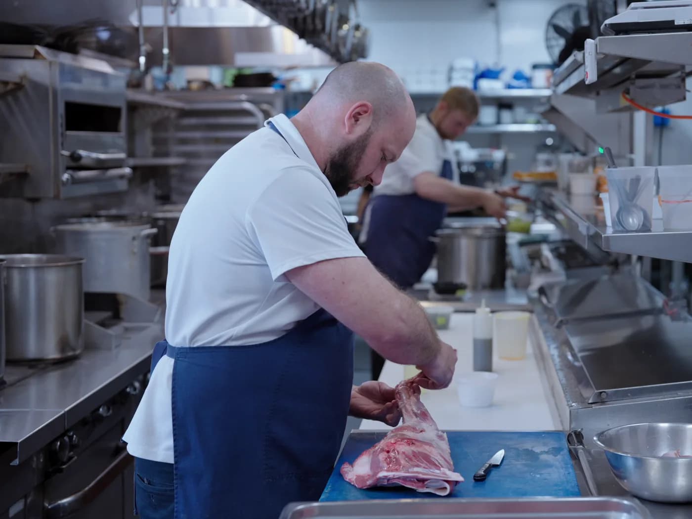 A chef preparing meat in a working restaurant kitchen