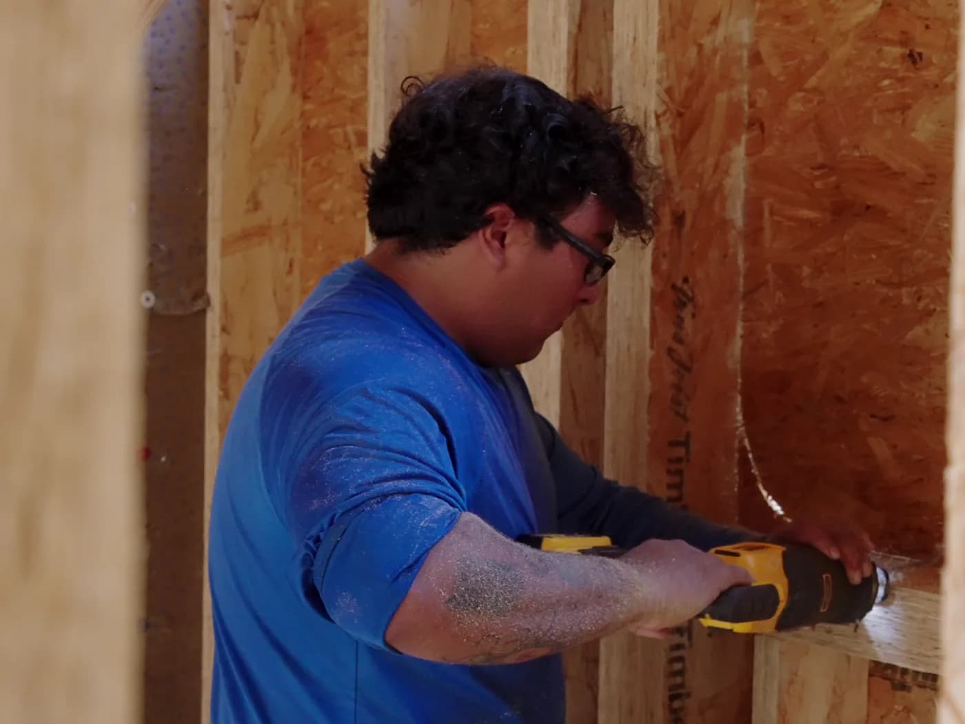 A tradesperson cutting into a wooden wall frame